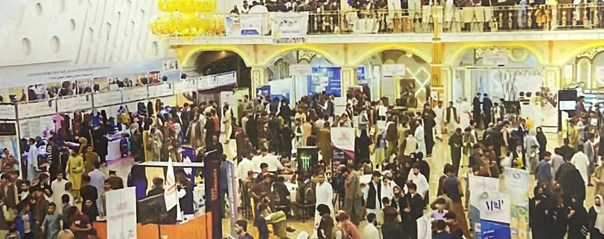 Crowds of visitors walking between stalls in the exhibition hall in Kabul